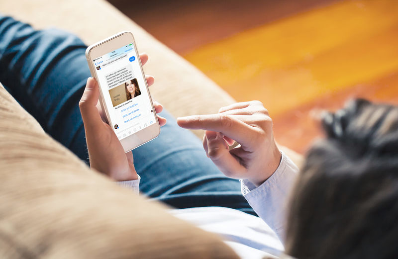Neukunde sitzt auf Sofa und schreibt mit Chatbot